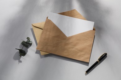 Photo of Kraft paper envelopes with letter, fountain pen and eucalyptus branch on grey background, flat lay. Mockup for design