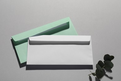 Paper envelopes and eucalyptus branch on grey background, flat lay. Mockup for design