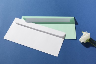 Photo of Paper envelopes and flower on blue background, above view. Mockup for design