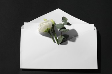 Paper envelope with letter, flowers and eucalyptus branch on black background, above view. Mockup for design