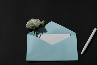 Photo of Paper envelope with letter, flowers and pen on black background, above view. Mockup for design