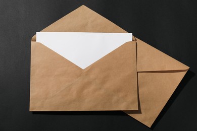 Photo of Kraft paper envelopes with letter on black background, top view. Mockup for design