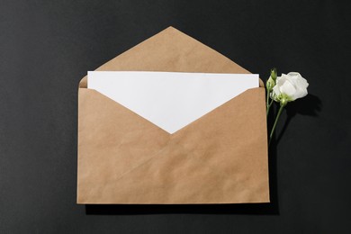 Photo of Kraft paper envelope with letter and flower on black background, above view. Mockup for design