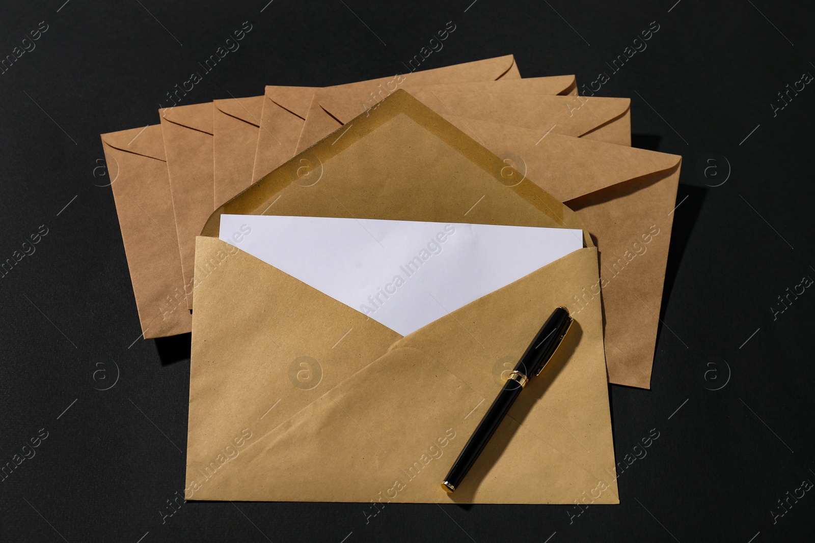 Photo of Kraft paper envelopes with letter and fountain pen on black background, above view. Mockup for design