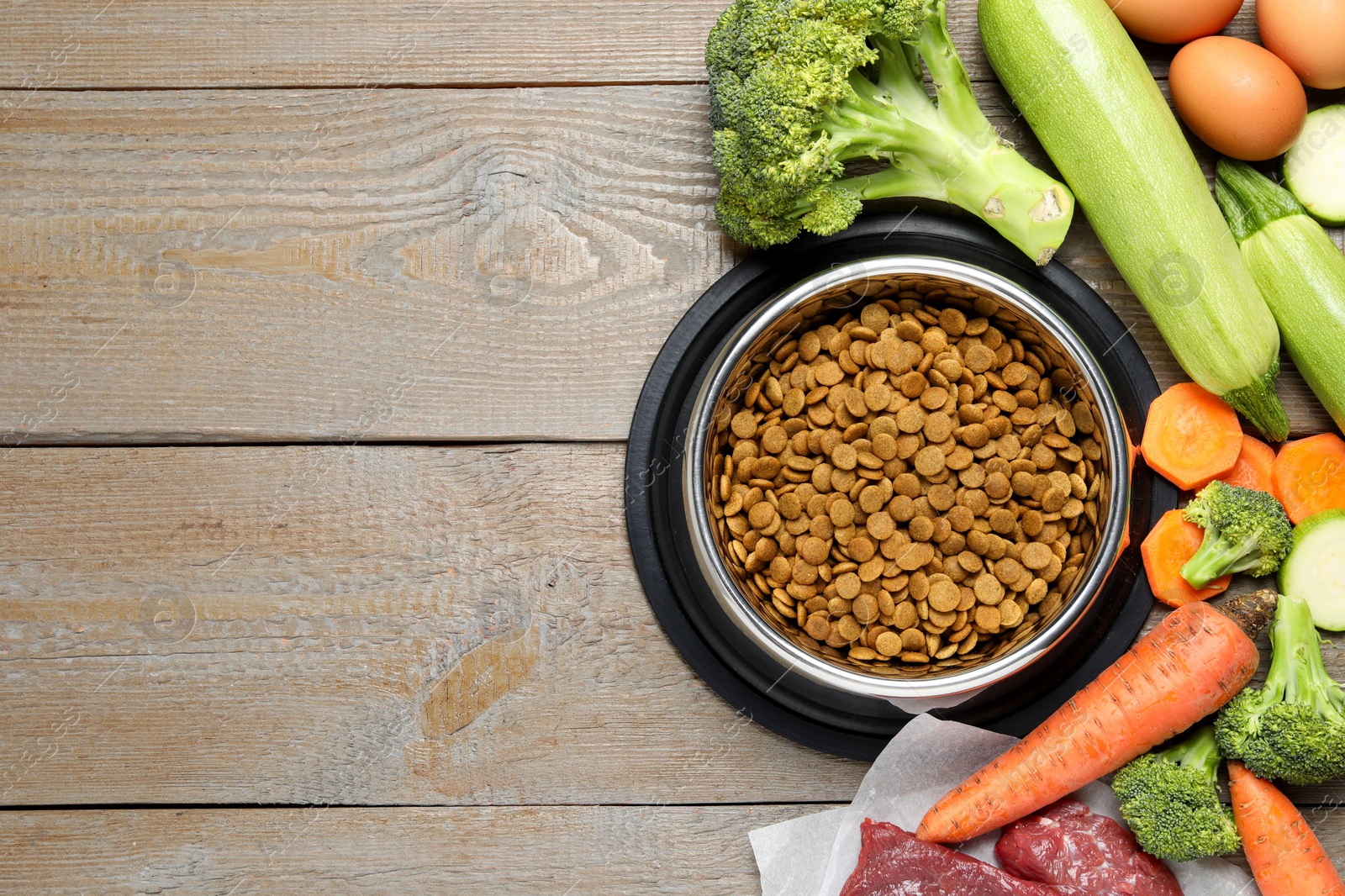 Photo of Dry pet food in feeding bowl and natural products on wooden table, flat lay. Space for text