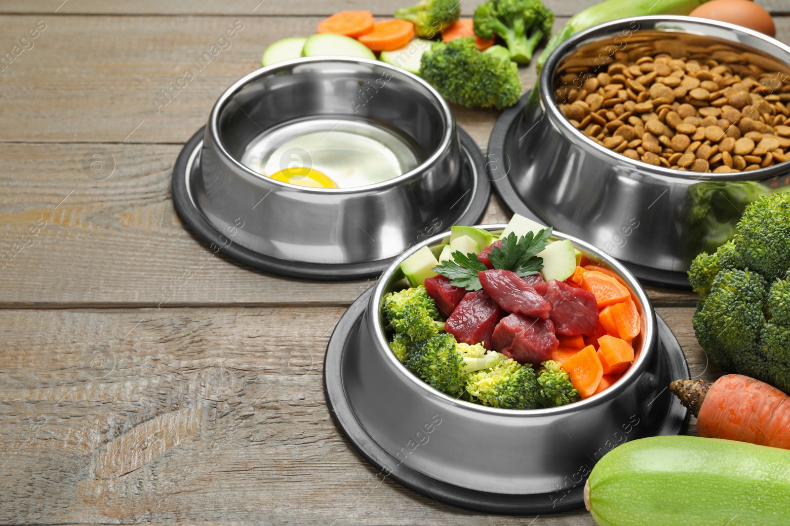 Photo of Dry and natural pet food in feeding bowls on wooden table, closeup. Space for text