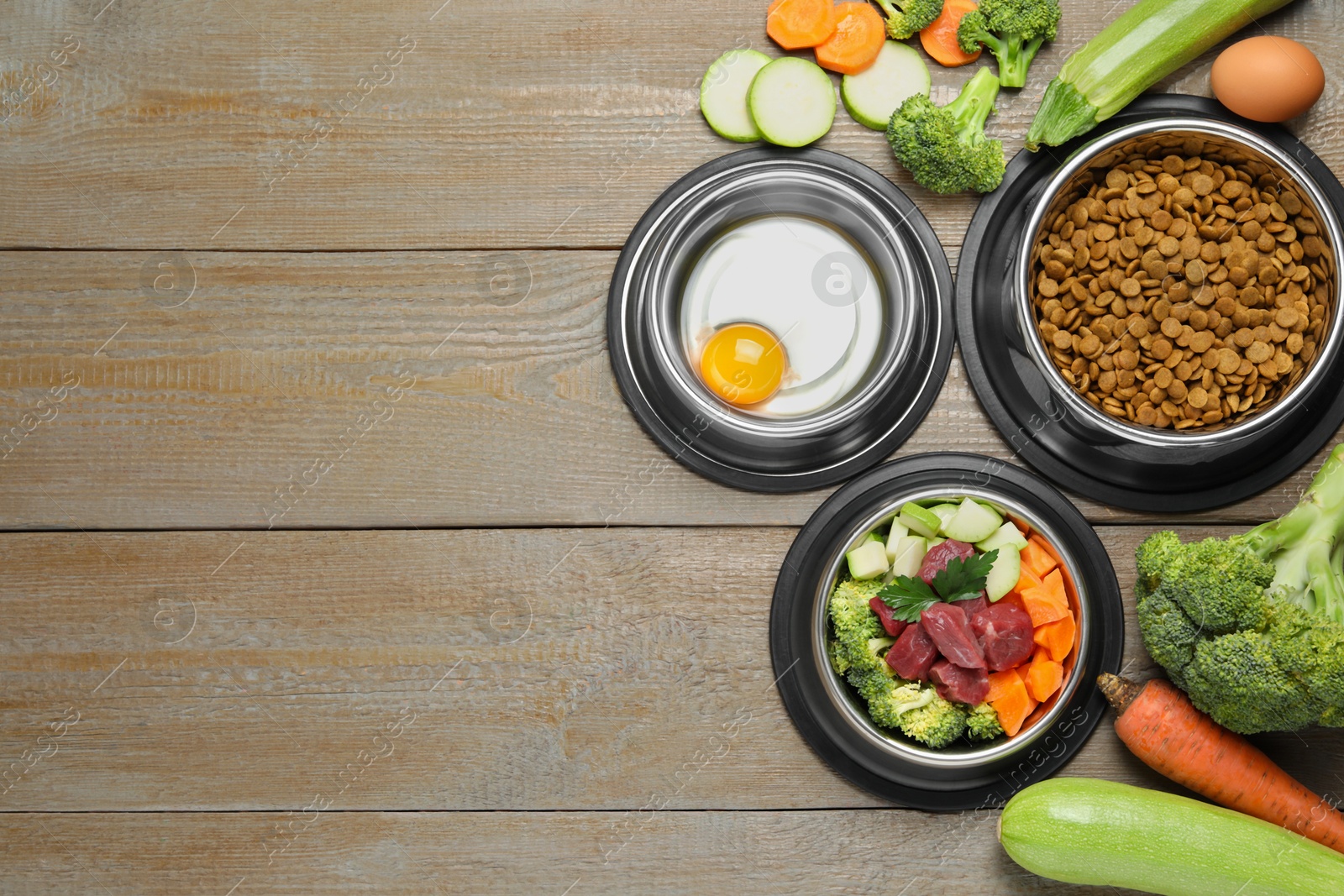 Photo of Dry and natural pet food in feeding bowls on wooden table, flat lay. Space for text