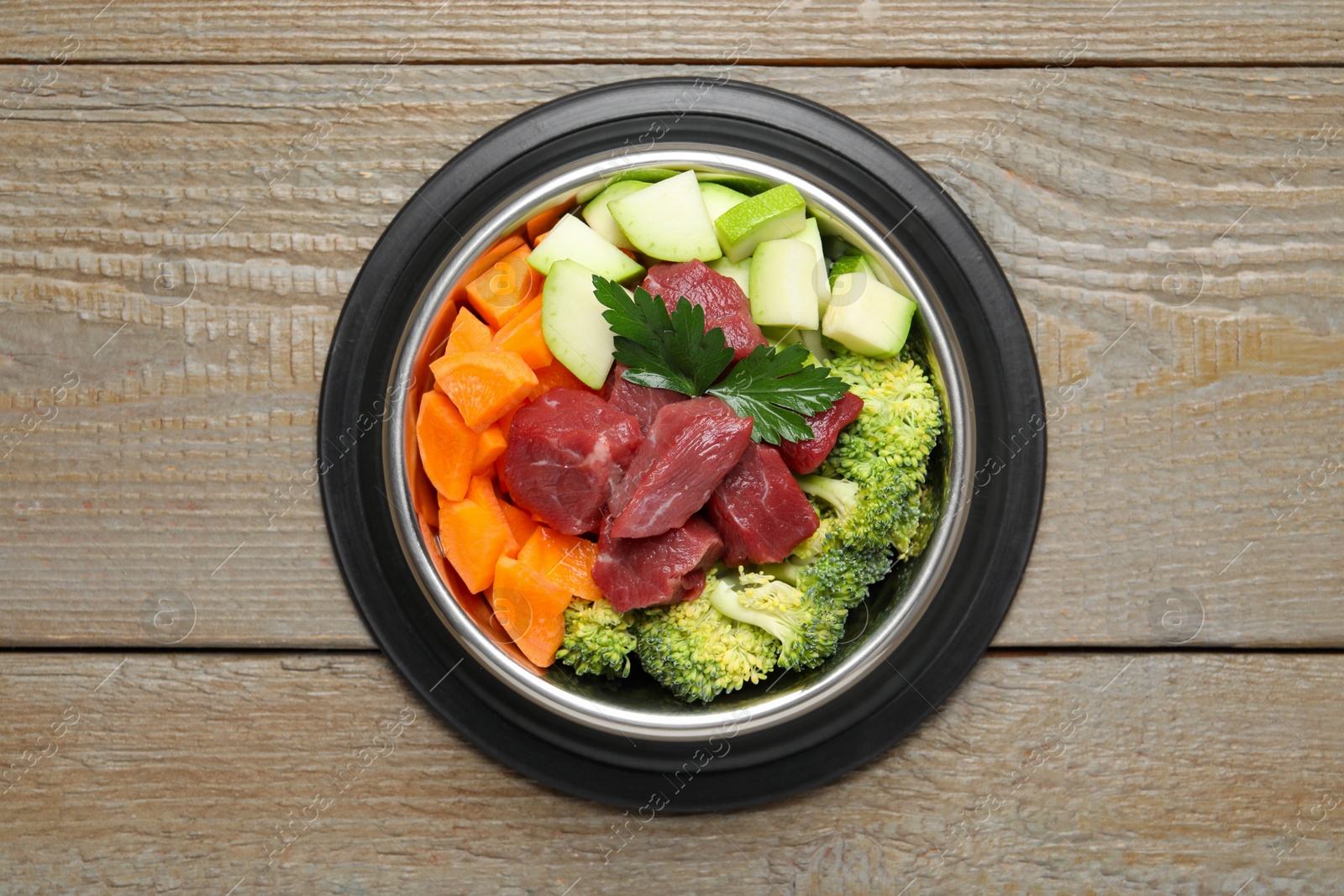 Photo of Fresh natural pet food in feeding bowl on wooden table, top view