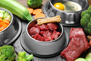 Photo of Pet food. Fresh beef in feeding bowl and chew bone among products on table, closeup