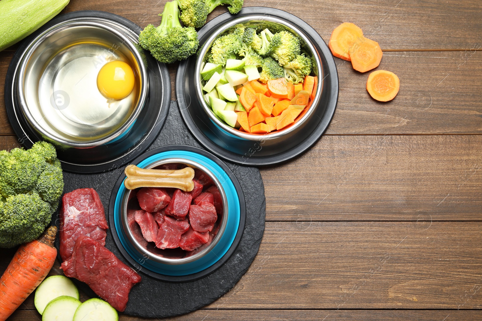 Photo of Natural pet food in feeding bowls and products on wooden table, flat lay. Space for text