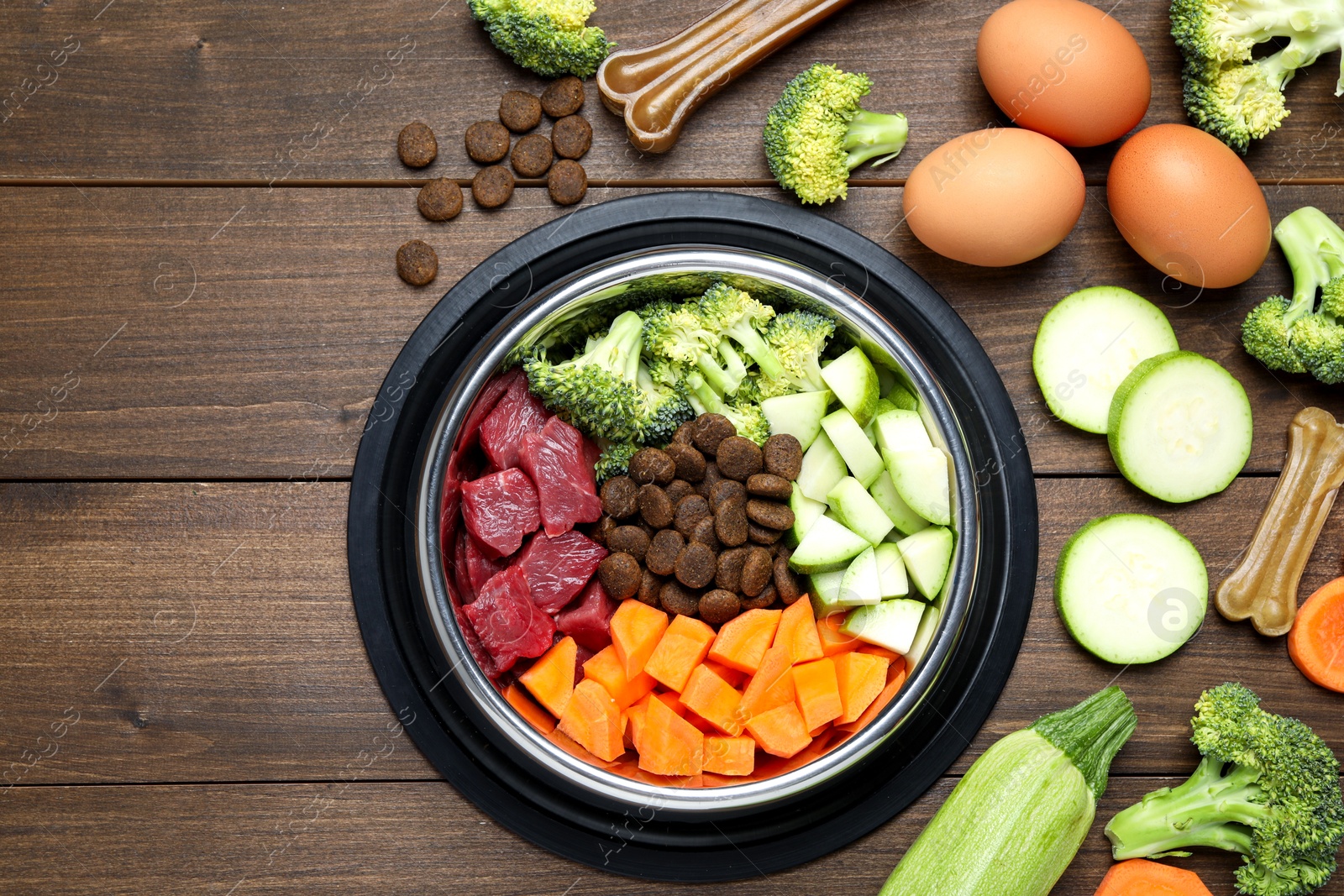 Photo of Dry and natural pet food in feeding bowl among products on wooden table, flat lay. Space for text