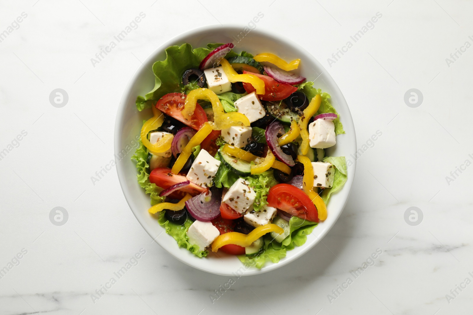 Photo of Delicious fresh Greek salad in bowl on white marble table, top view