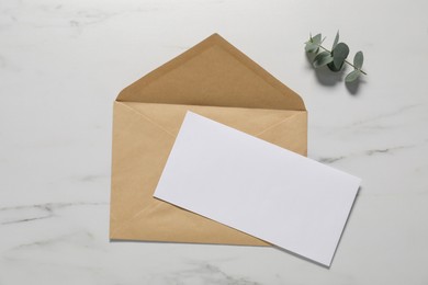 Photo of Kraft paper envelope with letter and eucalyptus branch on white marble background, flat lay. Mockup for design