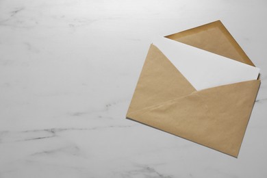 Photo of Kraft paper envelope with letter on white marble background, top view. Mockup for design