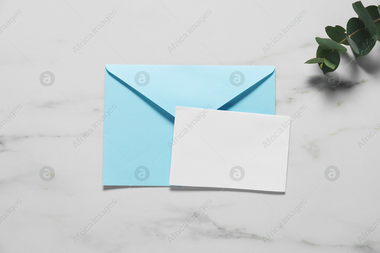 Photo of Paper envelope with letter and eucalyptus branch on white marble background, flat lay. Mockup for design