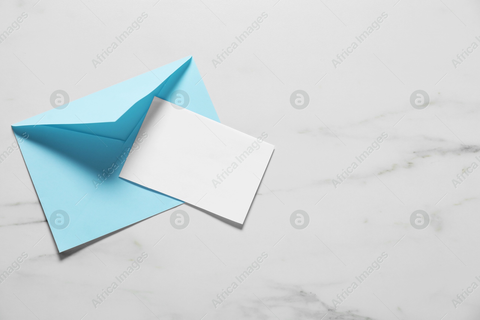 Photo of Paper envelope with letter on white marble background, top view. Mockup for design