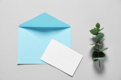 Paper envelope with letter and eucalyptus branch on gray background, flat lay. Mockup for design