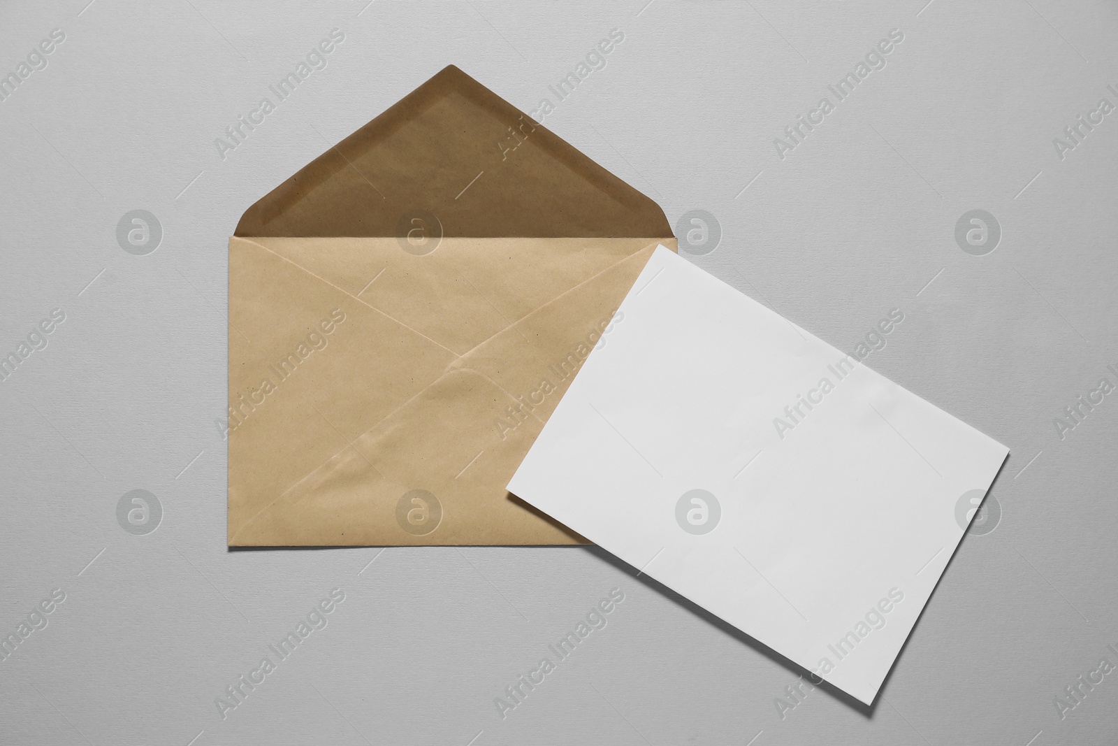 Photo of Kraft paper envelope with letter on gray background, top view. Mockup for design