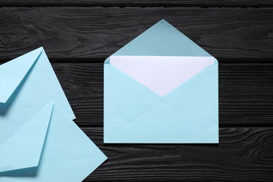 Photo of Paper envelopes with letter on black wooden background, flat lay. Mockup for design