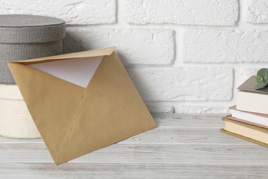 Photo of Kraft paper envelope with letter, boxes and books on wooden table near white brick wall. Mockup for design