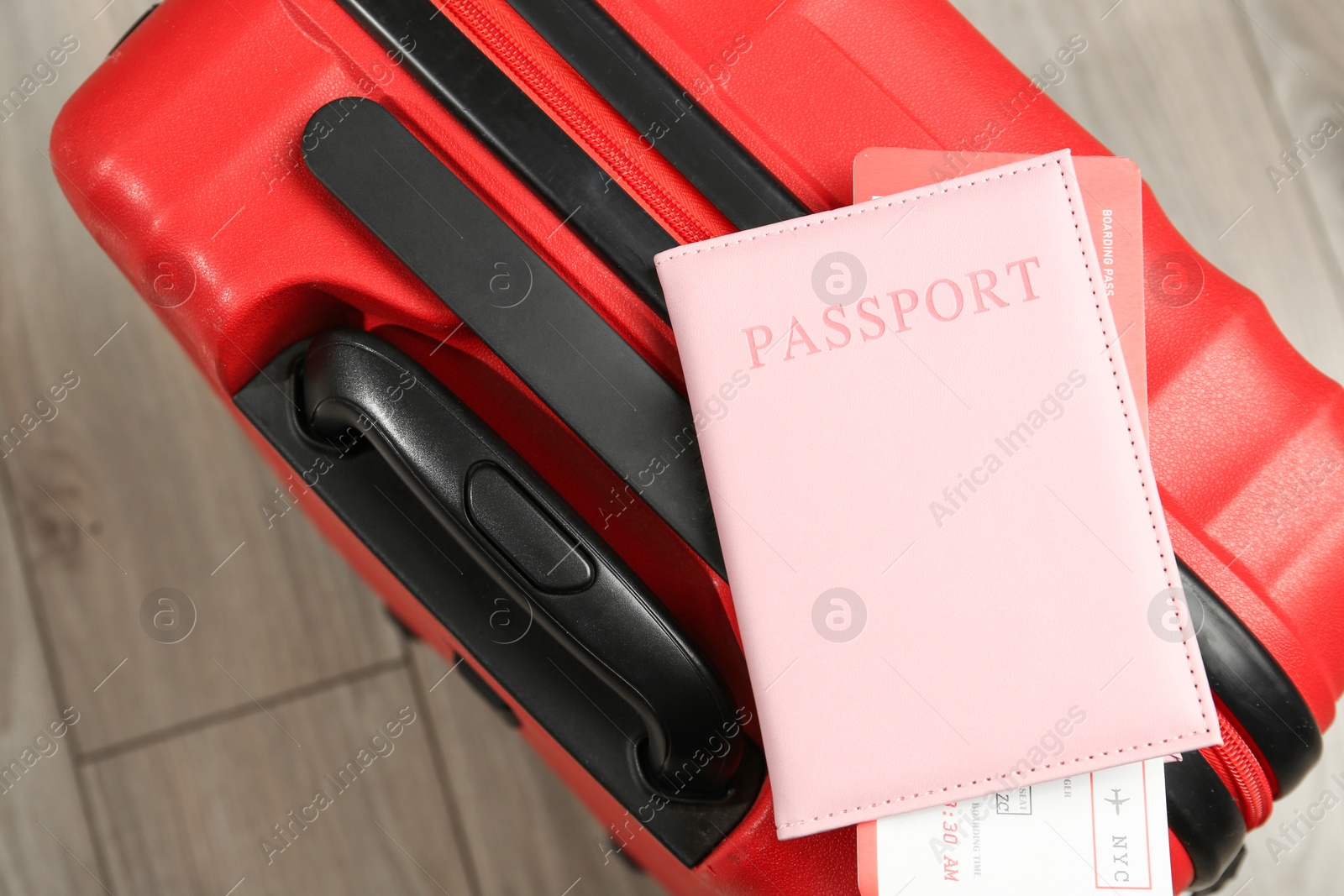 Photo of Passport with ticket and red suitcase on floor, top view