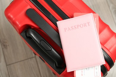 Photo of Passport with ticket and red suitcase on floor, top view