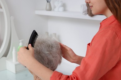 Photo of Granddaughter brushing her grandmother with comb at home, closeup