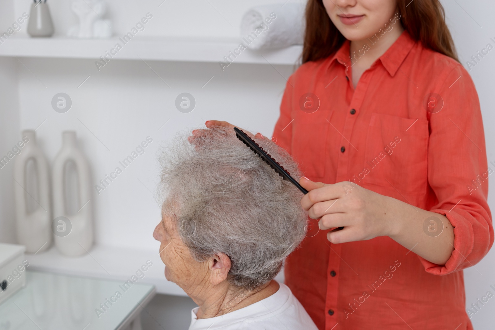 Photo of Granddaughter brushing her grandmother with comb at home, closeup