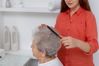 Photo of Granddaughter brushing her grandmother with comb at home, closeup