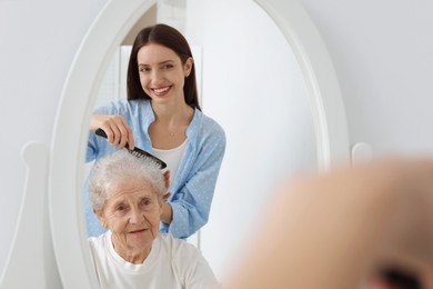 Photo of Woman brushing senior lady with comb indoors