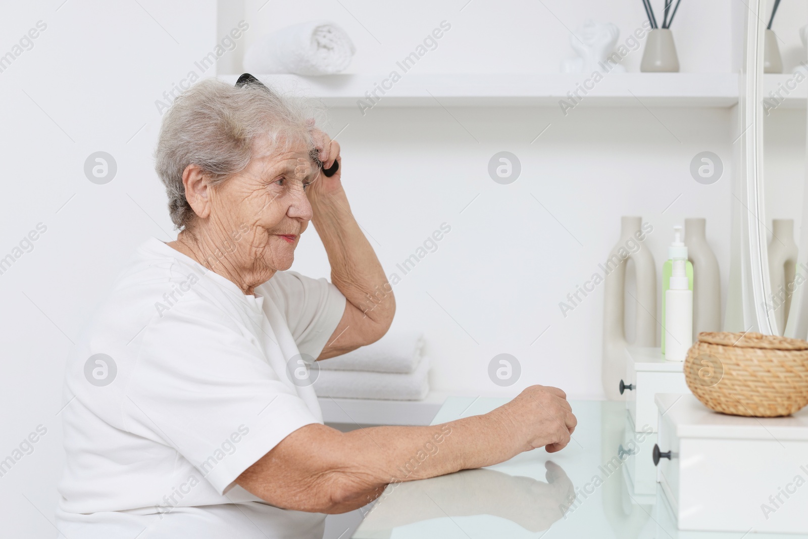 Photo of Senior woman brushing her hair with comb at dressing table indoors