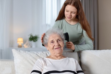 Granddaughter brushing her grandmother with comb at home