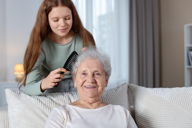 Photo of Granddaughter brushing her grandmother with comb at home. Space for text