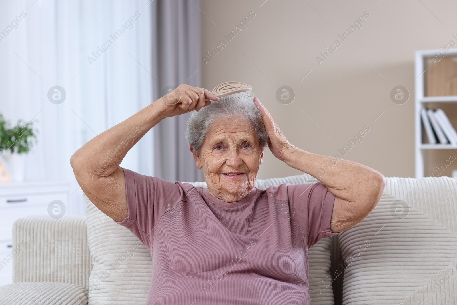 Photo of Senior woman brushing her hair with brush on sofa at home