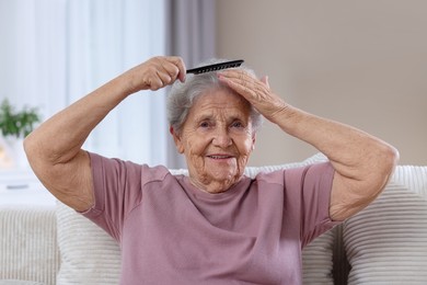 Photo of Senior woman brushing her hair with comb on sofa at home