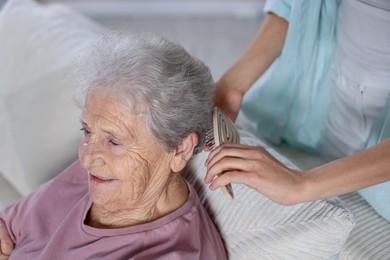 Photo of Woman brushing senior lady with brush indoors, closeup