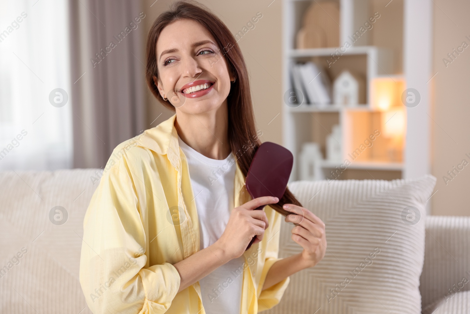 Photo of Smiling woman brushing her hair at home