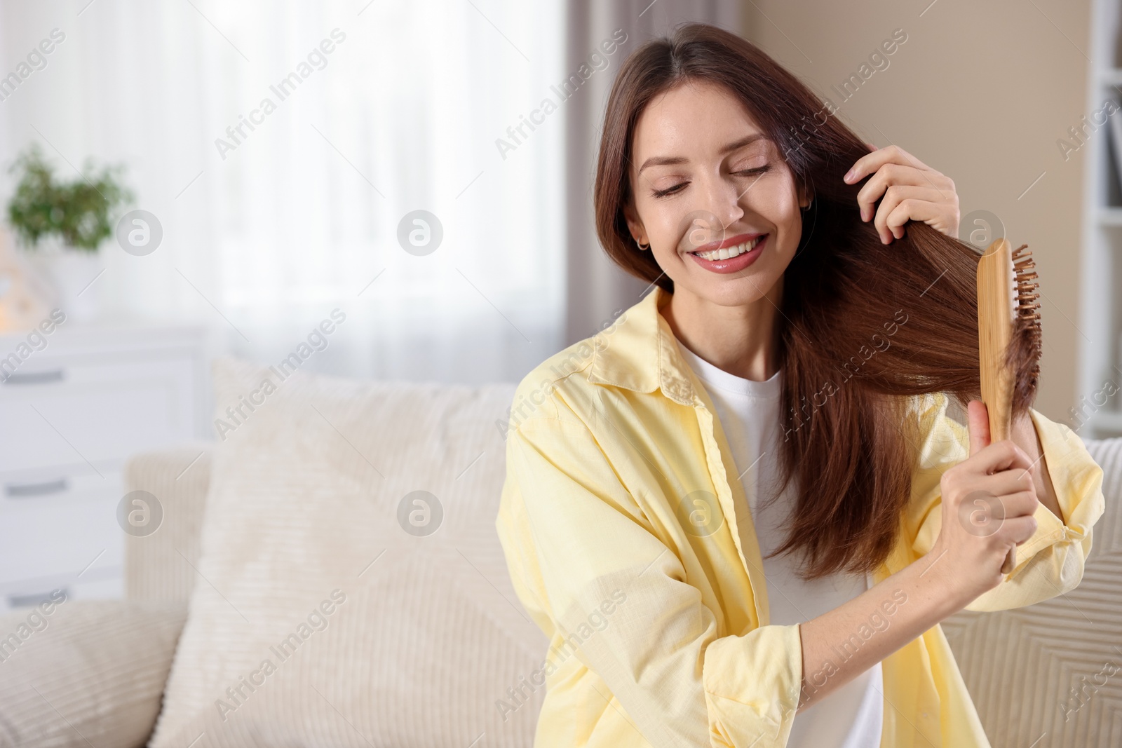 Photo of Smiling woman brushing her hair at home, space for text