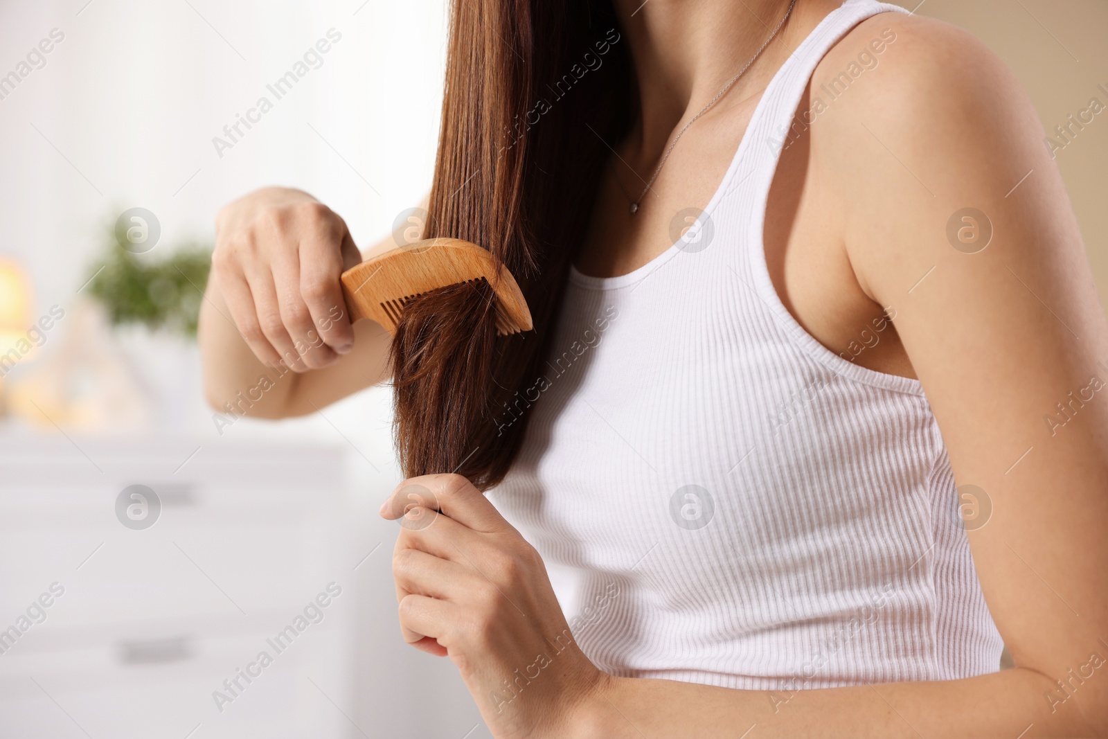 Photo of Woman brushing her hair with comb at home, closeup