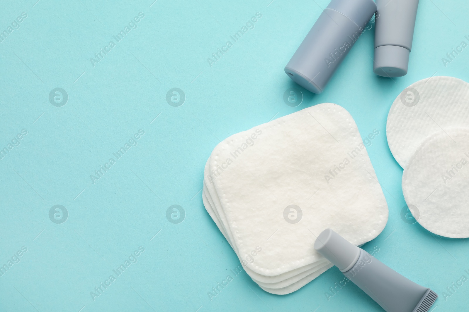 Photo of Clean cotton pads and cosmetic products on light blue background, flat lay. Space for text