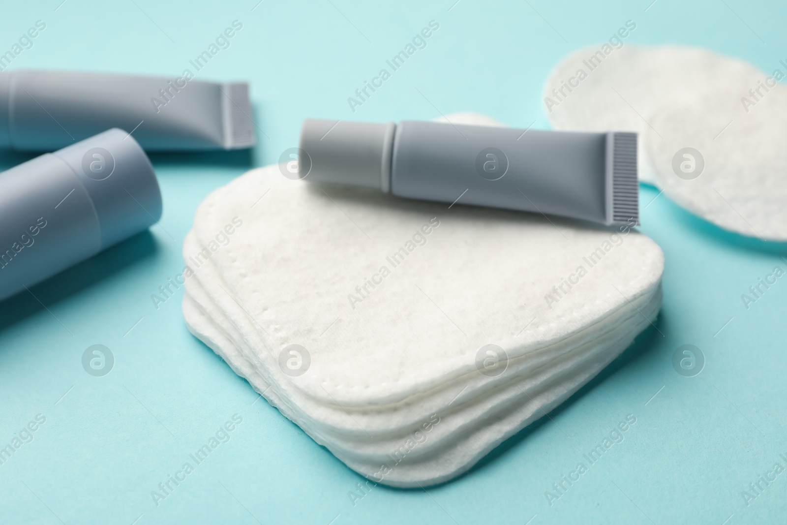 Photo of Clean cotton pads and cosmetic products on light blue background, closeup