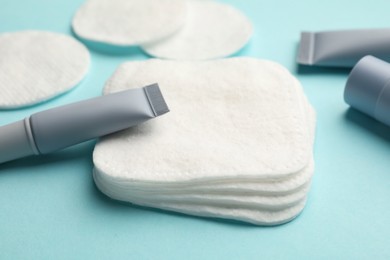 Photo of Clean cotton pads and cosmetic products on light blue background, closeup