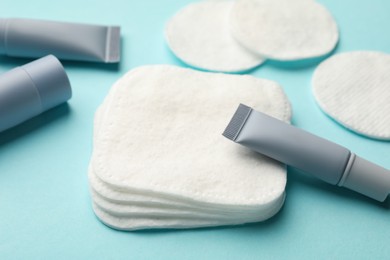 Photo of Clean cotton pads and cosmetic products on light blue background, closeup