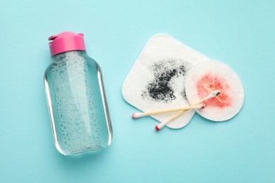 Photo of Dirty cotton pads, swabs and micellar water on light blue background, top view