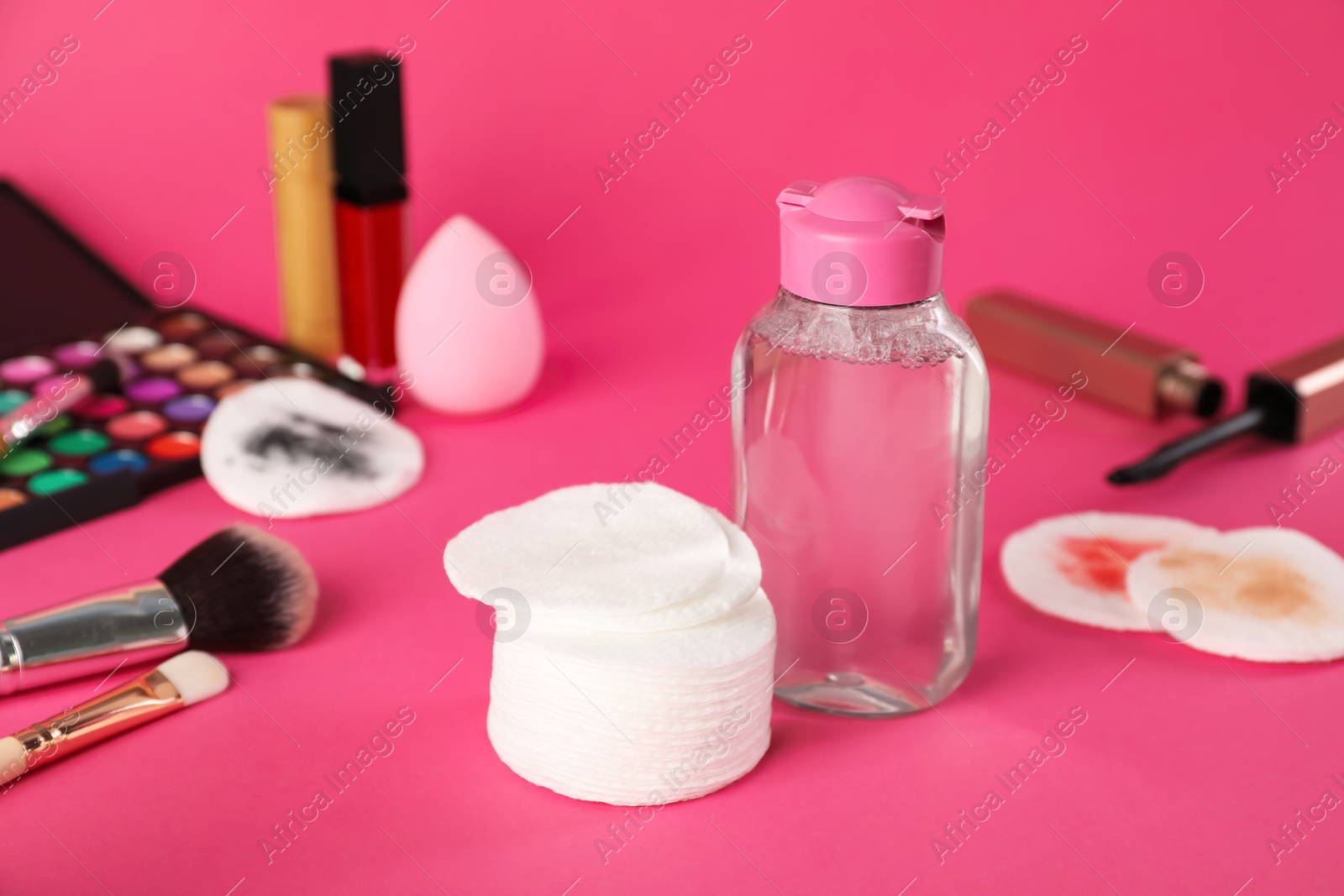 Photo of Cotton pads, micellar water and makeup products on pink background, closeup