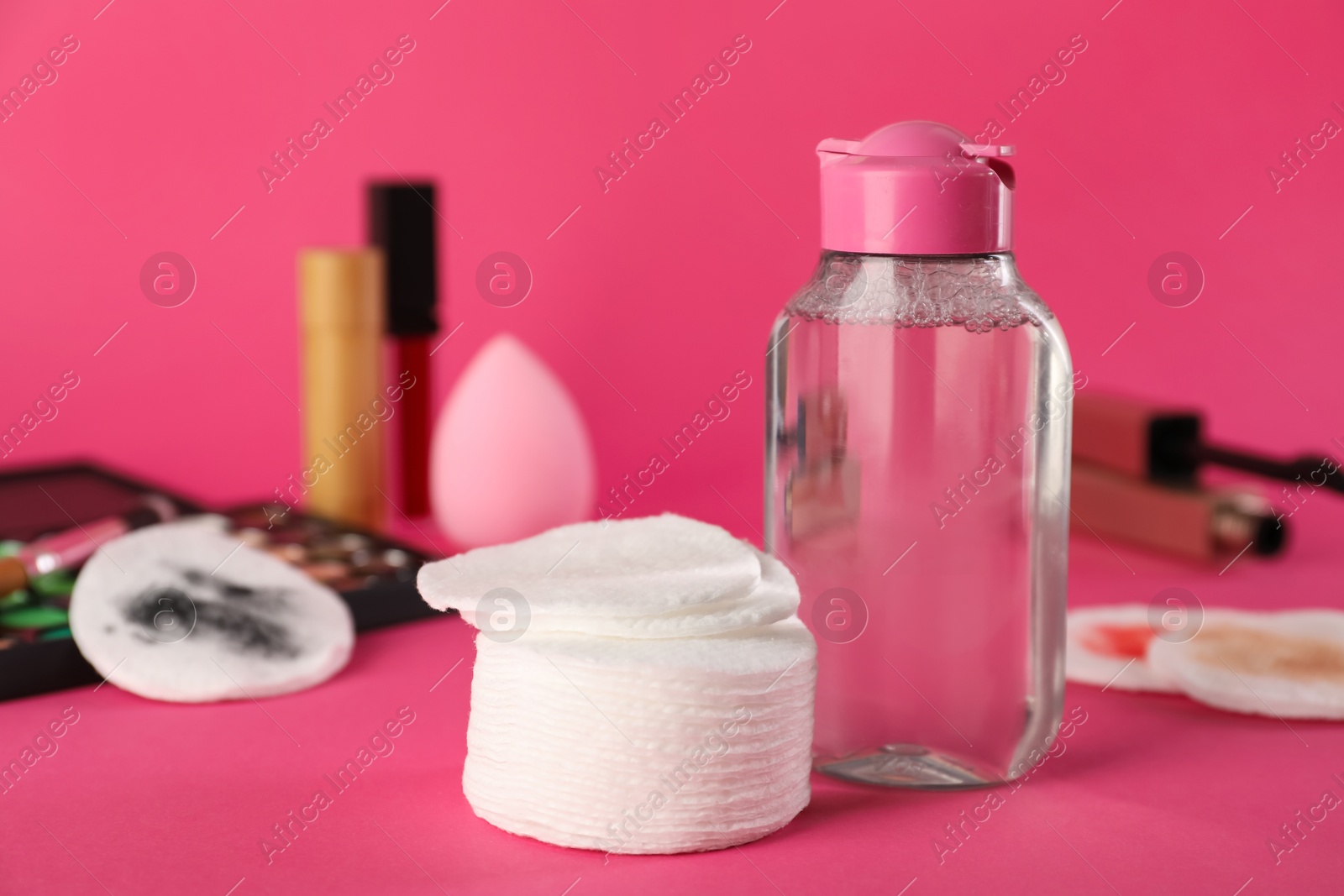 Photo of Cotton pads, micellar water and makeup products on pink background, closeup