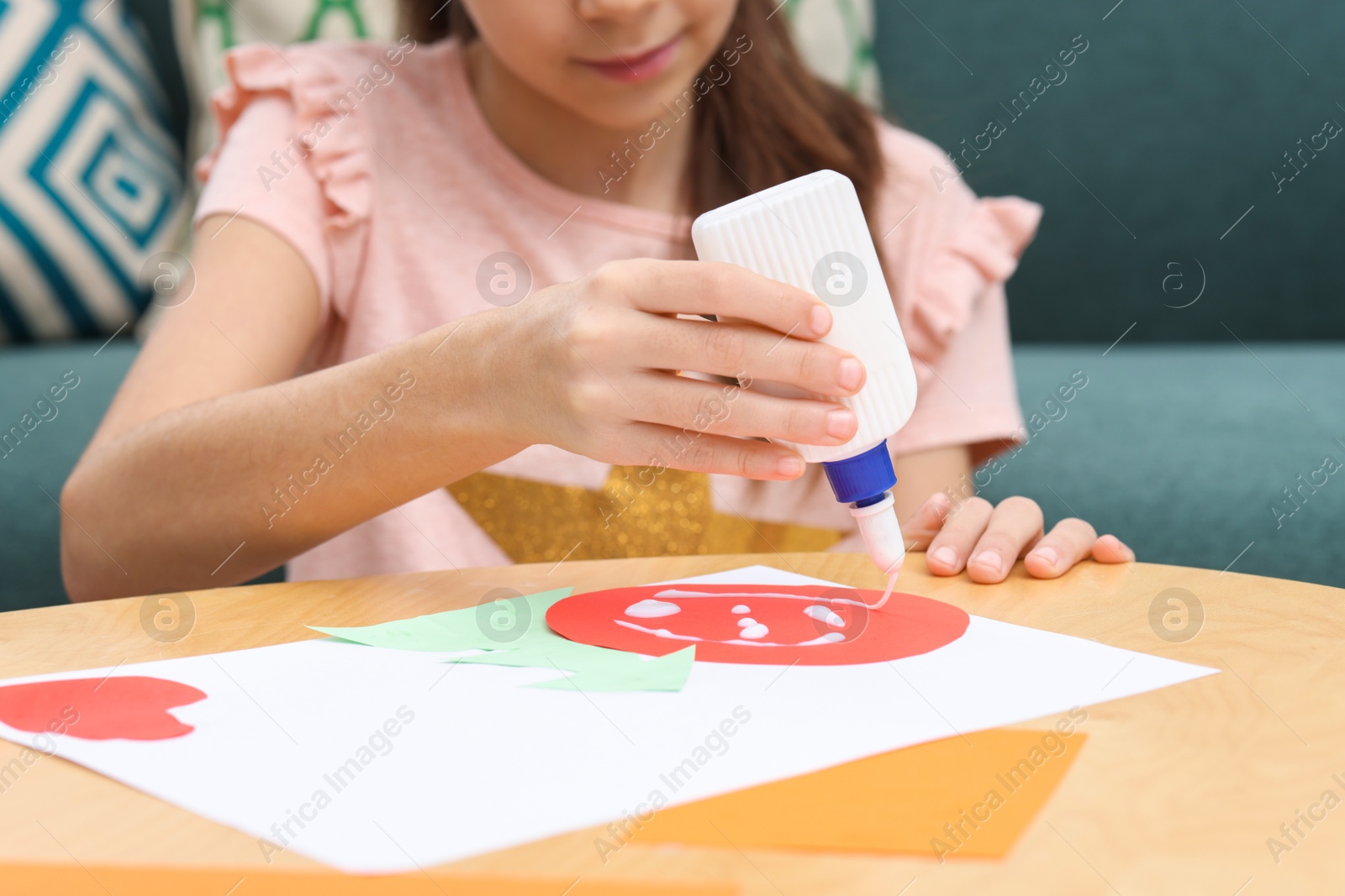 Photo of Girl applying glue onto paper figure for her creative project at table indoors, closeup. Art and craft