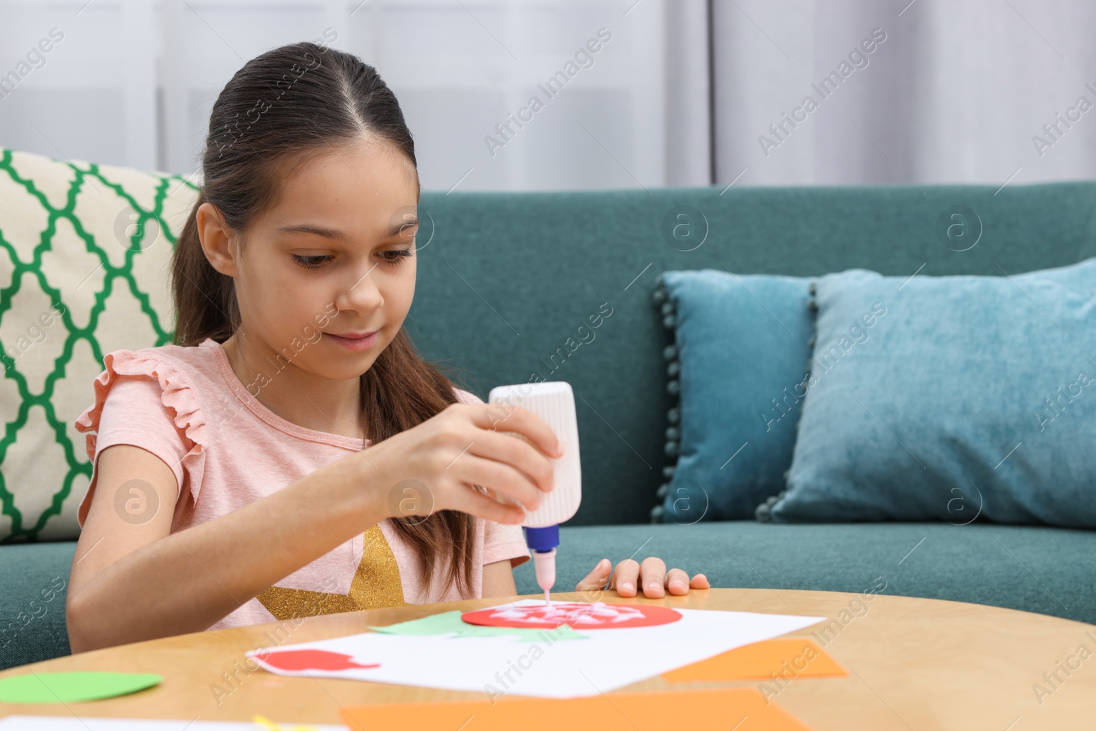 Photo of Girl applying glue onto paper figure for her creative project at table indoors. Art and craft