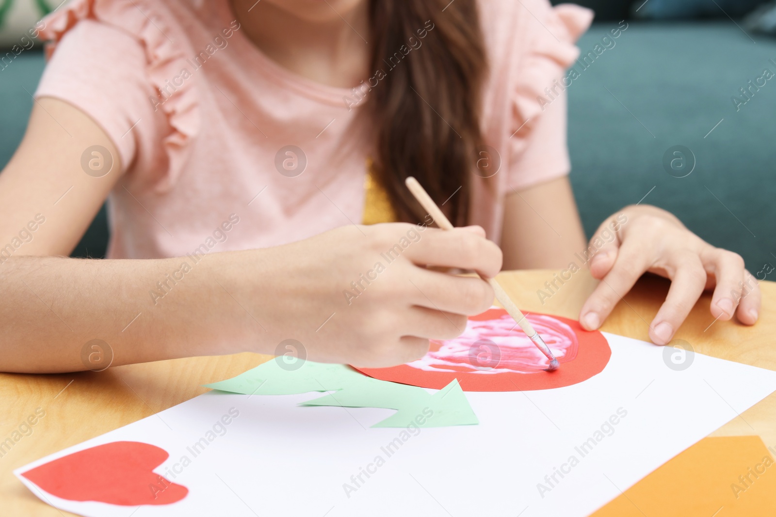 Photo of Girl applying glue onto paper figure for her creative project at table indoors, closeup. Art and craft