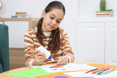 Photo of Girl applying glue onto paper figure for her creative project at table indoors. Art and craft